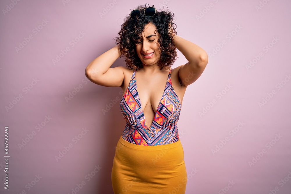 Young beautiful arab woman on vacation wearing swimsuit and sunglasses over pink background suffering from headache desperate and stressed because pain and migraine. Hands on head. Young beautiful arab woman on vacation wearing swimsuit and sunglasses over pink background suffering from headache desperate and stressed because pain and migraine. Hands on head.