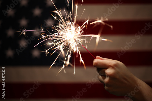 Hand holding lit sparkler in front of the American Flag for 4th of July celebration