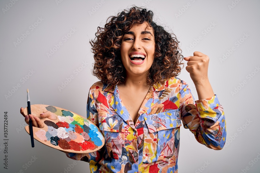Young beautiful curly arab artist woman painting using brush and palette with colors screaming proud and celebrating victory and success very excited, cheering emotion - obrazy, fototapety, plakaty 