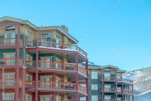 Houses with snowy roofs and balconies against blue sky and frosty mountain