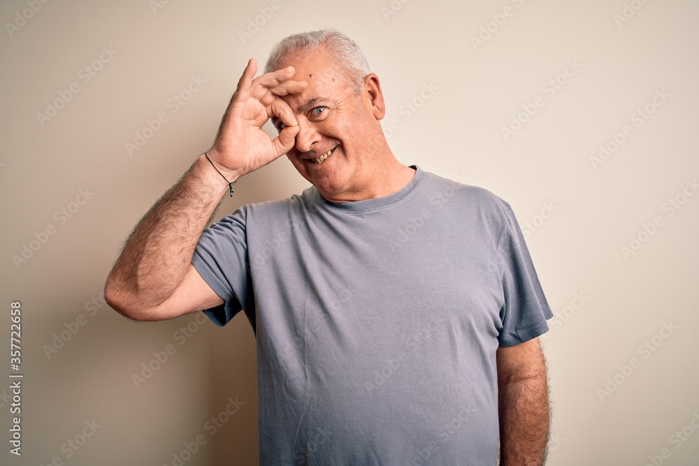 Middle age handsome hoary man wearing t-shirt standing over isolated white background doing ok gesture with hand smiling, eye looking through fingers with happy face.