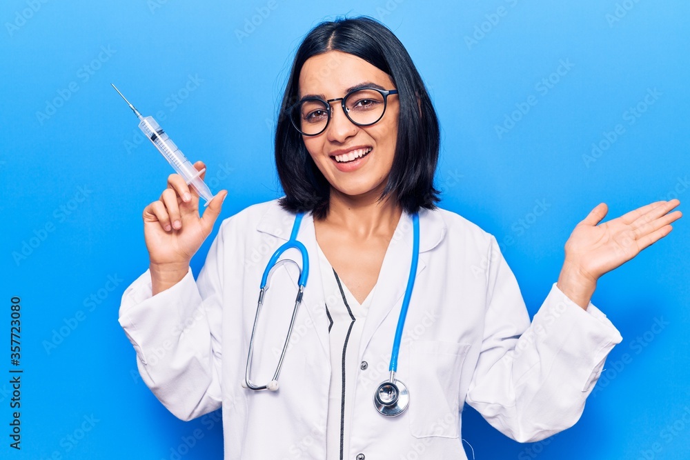 Young beautiful latin woman wearing doctor stethoscope holding syringe celebrating victory with happy smile and winner expression with raised hands Young beautiful latin woman wearing doctor stethoscope holding syringe celebrating victory with happy smile and winner expression with raised hands