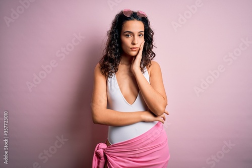 Beautiful woman with curly hair on vacation wearing white swimsuit over pink background thinking looking tired and bored with depression problems with crossed arms. © Krakenimages.com