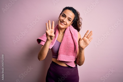 Young beautiful sportswoman with curly hair doing sport using towel over pink background showing and pointing up with fingers number eight while smiling confident and happy.