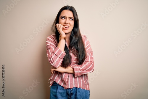 Young brunette woman wearing casual striped shirt over isolated background looking stressed and nervous with hands on mouth biting nails. Anxiety problem. © Krakenimages.com