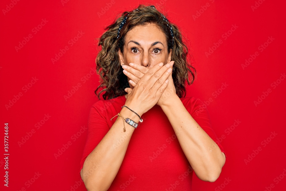 Middle age senior brunette woman wearing casual t-shirt standing over red background shocked covering mouth with hands for mistake. Secret concept. Middle age senior brunette woman wearing casual t-shirt standing over red background shocked covering mouth with hands for mistake. Secret concept.