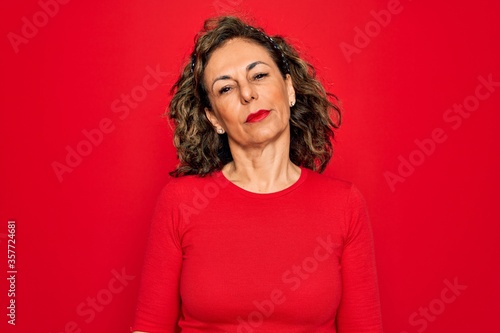 Middle age senior brunette woman wearing casual t-shirt standing over red background Relaxed with serious expression on face. Simple and natural looking at the camera.