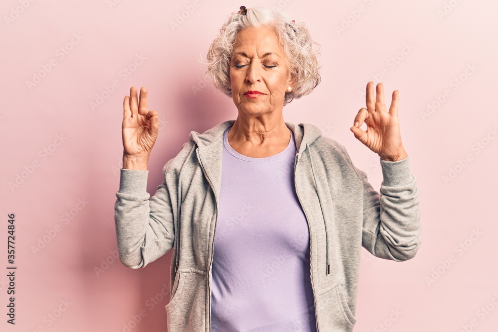 Senior grey-haired woman wearing casual sporty clothes relax and smiling with eyes closed doing meditation gesture with fingers. yoga concept. Senior grey-haired woman wearing casual sporty clothes relax and smiling with eyes closed doing meditation gesture with fingers. yoga concept.