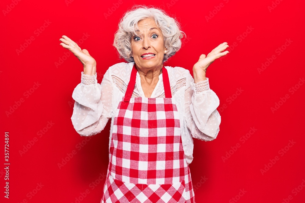 Senior grey-haired woman wearing apron clueless and confused with open arms, no idea and doubtful face. Senior grey-haired woman wearing apron clueless and confused with open arms, no idea and doubtful face.
