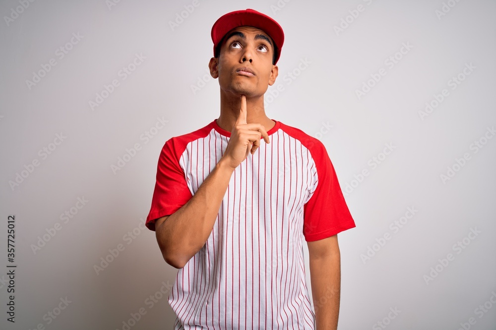 Young handsome african american sportsman wearing striped baseball t-shirt and cap Thinking concentrated about doubt with finger on chin and looking up wondering Young handsome african american sportsman wearing striped baseball t-shirt and cap Thinking concentrated about doubt with finger on chin and looking up wondering