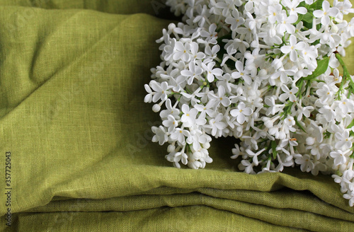 The linen green fabric is folded on the kitchen table. There is also a sprig of white lilac on the table. The delicate details of the home interior are in line with the trends in eco-fashion.