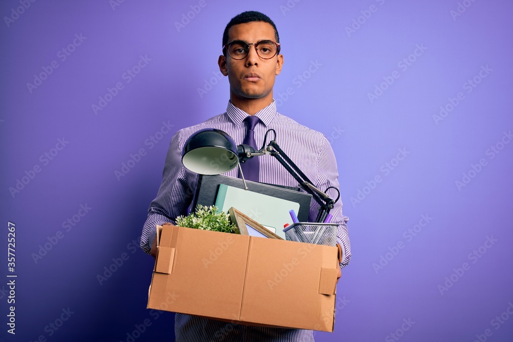 Handsome african american man fired holding box with work objects over purple background with a confident expression on smart face thinking serious Handsome african american man fired holding box with work objects over purple background with a confident expression on smart face thinking serious