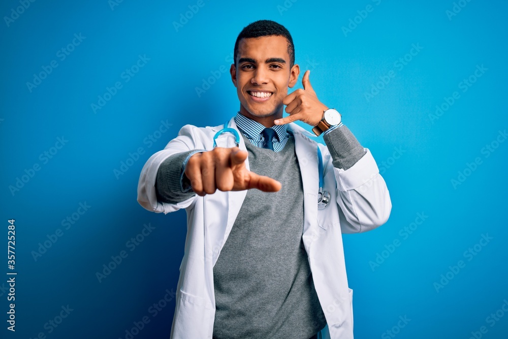 Handsome african american doctor man wearing coat and stethoscope over blue background smiling doing talking on the telephone gesture and pointing to you. Call me. Handsome african american doctor man wearing coat and stethoscope over blue background smiling doing talking on the telephone gesture and pointing to you. Call me.