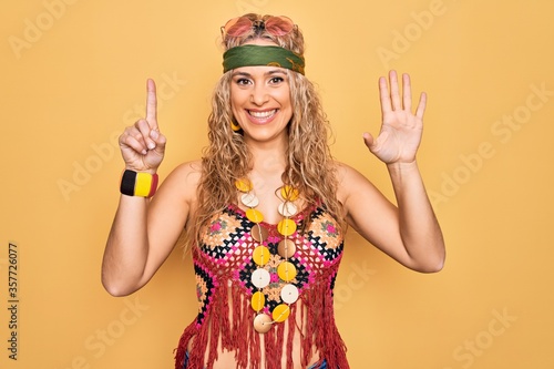Beautiful blonde hippie woman wearing sunglasses and accessories over yellow background showing and pointing up with fingers number six while smiling confident and happy.