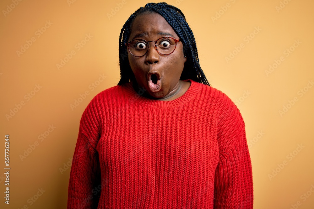 African american plus size woman with braids wearing casual sweater over yellow background afraid and shocked with surprise expression, fear and excited face. African american plus size woman with braids wearing casual sweater over yellow background afraid and shocked with surprise expression, fear and excited face.