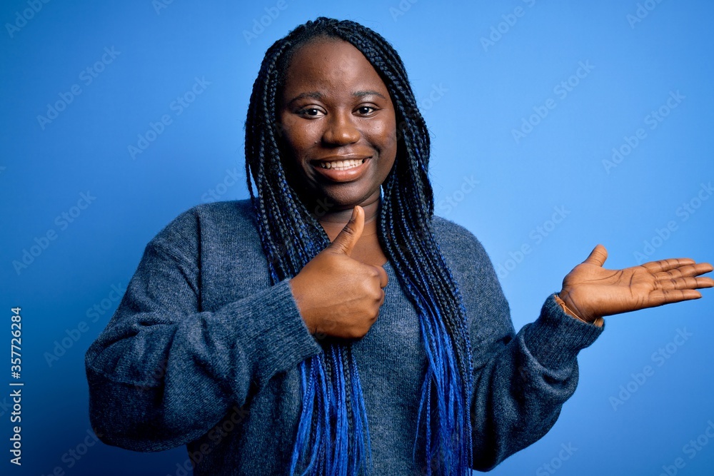 African american plus size woman with braids wearing casual sweater over blue background Showing palm hand and doing ok gesture with thumbs up, smiling happy and cheerful African american plus size woman with braids wearing casual sweater over blue background Showing palm hand and doing ok gesture with thumbs up, smiling happy and cheerful