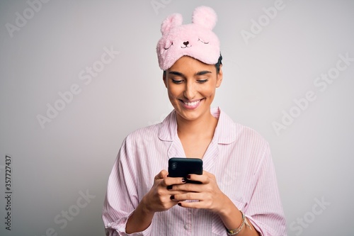 Young beautiful woman wearing pajama and sleep mask having conversation using smartphone with a happy face standing and smiling with a confident smile showing teeth © Krakenimages.com