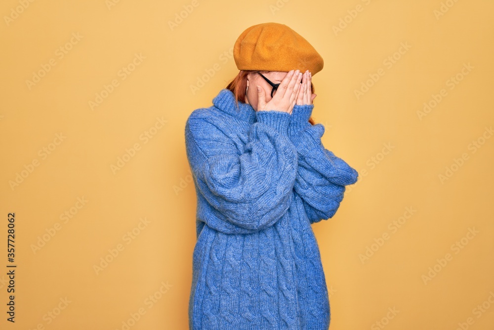 Young beautiful redhead woman wearing french beret and glasses over yellow background with sad expression covering face with hands while crying. Depression concept. Young beautiful redhead woman wearing french beret and glasses over yellow background with sad expression covering face with hands while crying. Depression concept.