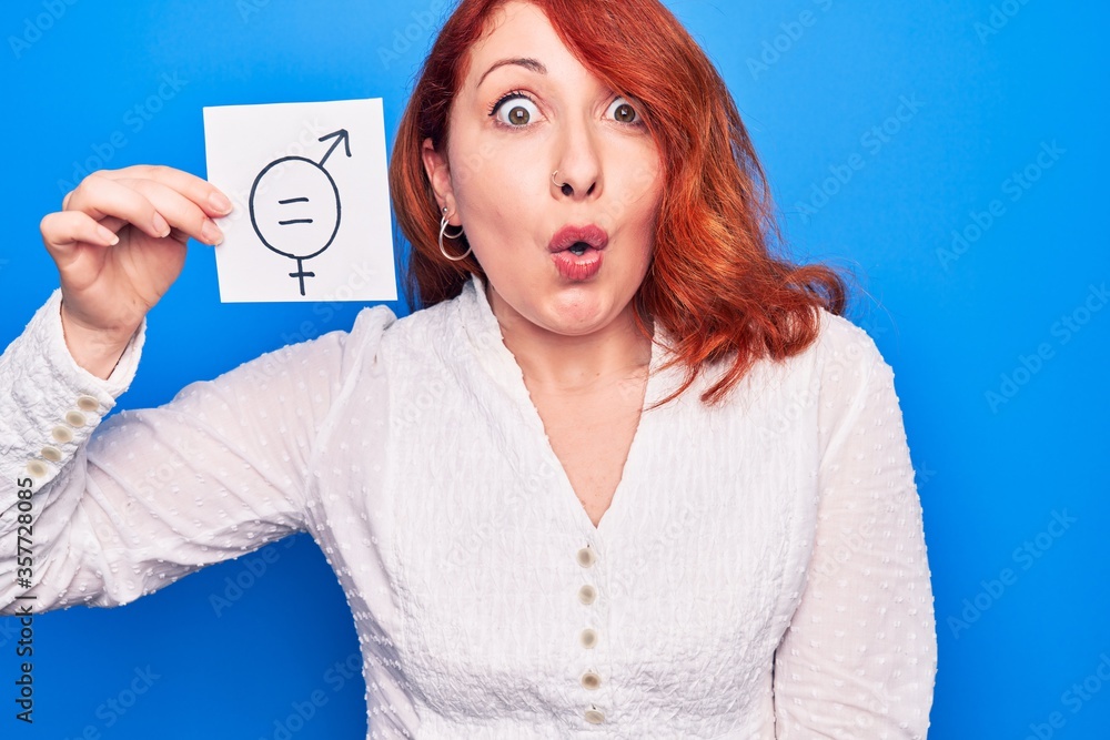Young redhead woman asking for sex discrimination holding paper with gender equality message scared and amazed with open mouth for surprise, disbelief face Young redhead woman asking for sex discrimination holding paper with gender equality message scared and amazed with open mouth for surprise, disbelief face