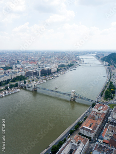 Aerial view of Széchenyi Chain Bridge over Danube river near Parliament palace in Budapest city, Hungary. Cars drive on bridge, road, boats floating on river, ships moored near riverside. Historic cen © dimabucci