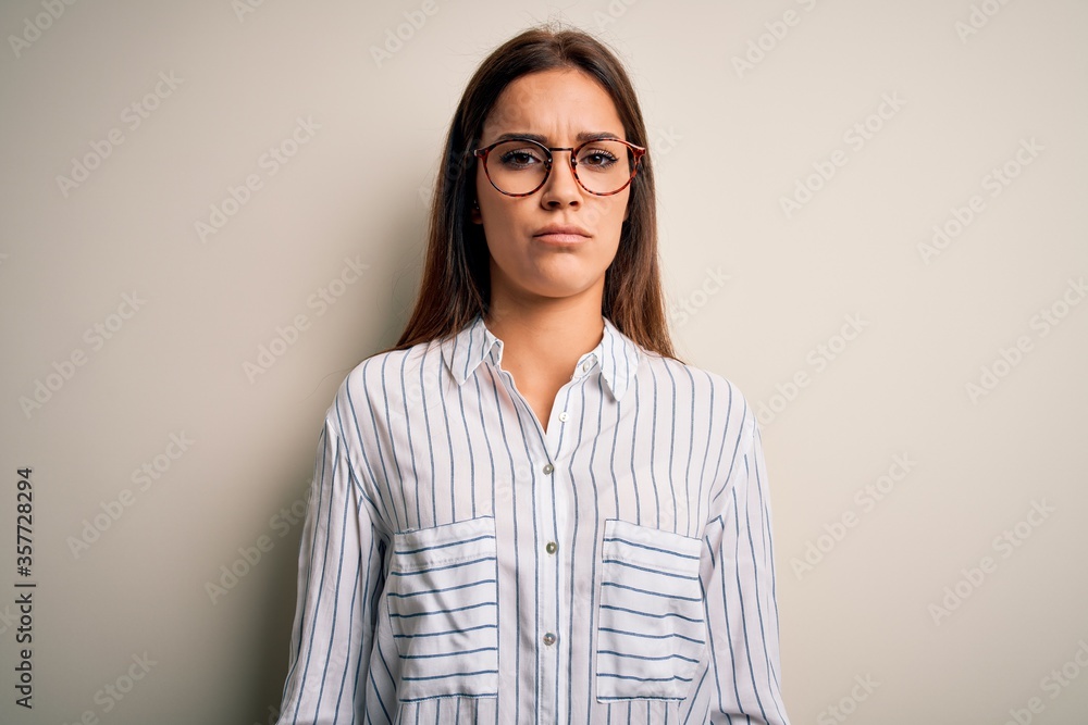 Young beautiful brunette woman wearing casual shirt and glasses over white background skeptic and nervous, frowning upset because of problem. Negative person. Young beautiful brunette woman wearing casual shirt and glasses over white background skeptic and nervous, frowning upset because of problem. Negative person.