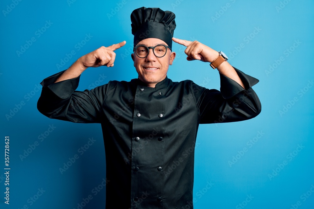 Middle age handsome grey-haired chef man wearing cooker uniform and hat smiling pointing to head with both hands finger, great idea or thought, good memory Middle age handsome grey-haired chef man wearing cooker uniform and hat smiling pointing to head with both hands finger, great idea or thought, good memory