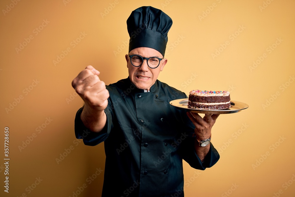 Middle age handsome grey-haired baker man wearing cooker uniform and hat holding cake annoyed and frustrated shouting with anger, crazy and yelling with raised hand, anger concept Middle age handsome grey-haired baker man wearing cooker uniform and hat holding cake annoyed and frustrated shouting with anger, crazy and yelling with raised hand, anger concept