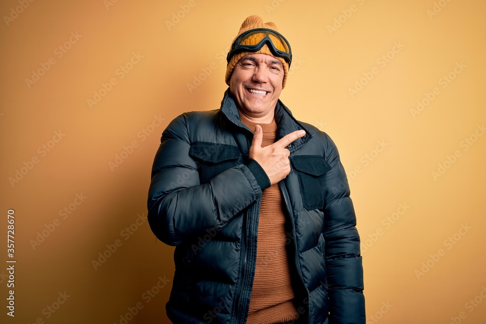 Middle age handsome grey-haired skier man on vacation wearing ski goggles cheerful with a smile of face pointing with hand and finger up to the side with happy and natural expression on face Middle age handsome grey-haired skier man on vacation wearing ski goggles cheerful with a smile of face pointing with hand and finger up to the side with happy and natural expression on face
