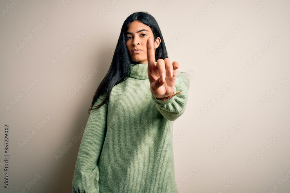 Young beautiful hispanic woman wearing green winter sweater over isolated background Pointing with finger up and angry expression, showing no gesture Young beautiful hispanic woman wearing green winter sweater over isolated background Pointing with finger up and angry expression, showing no gesture