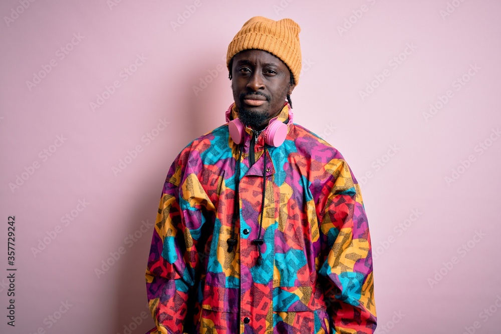 Young handsome african american man wearing colorful coat and cap over pink background skeptic and nervous, frowning upset because of problem. Negative person. Young handsome african american man wearing colorful coat and cap over pink background skeptic and nervous, frowning upset because of problem. Negative person.