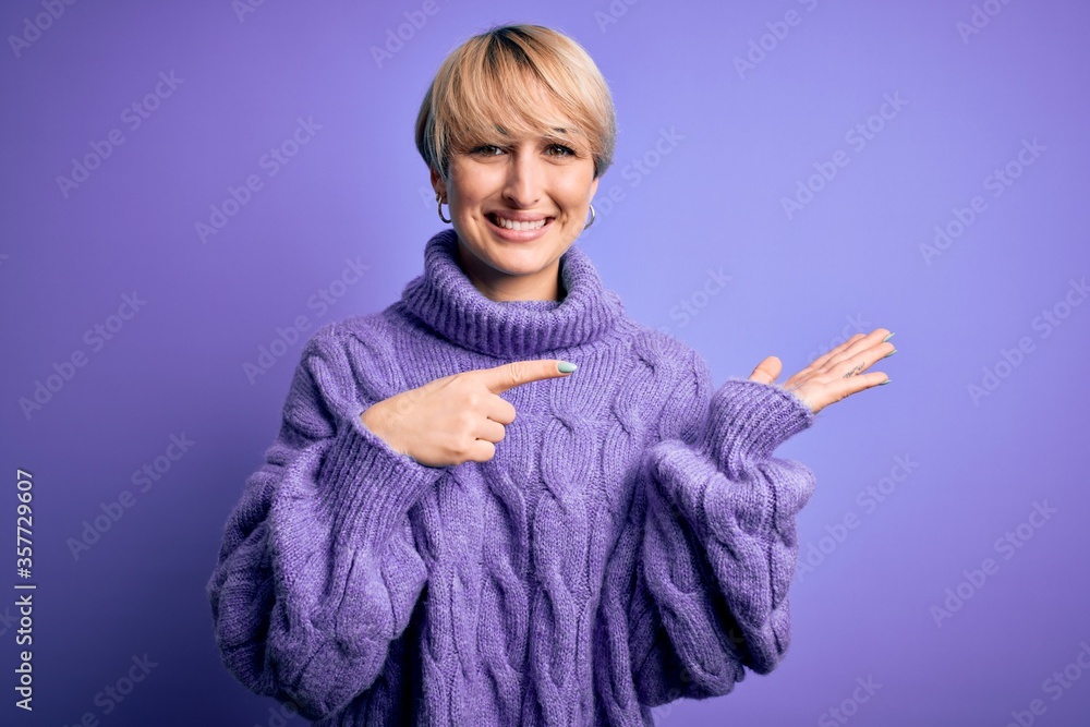 Young blonde woman with short hair wearing winter turtleneck sweater over purple background amazed and smiling to the camera while presenting with hand and pointing with finger. Young blonde woman with short hair wearing winter turtleneck sweater over purple background amazed and smiling to the camera while presenting with hand and pointing with finger.