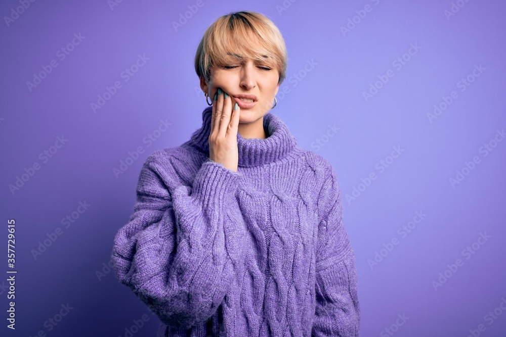 Young blonde woman with short hair wearing winter turtleneck sweater over purple background touching mouth with hand with painful expression because of toothache or dental illness on teeth. Dentist Young blonde woman with short hair wearing winter turtleneck sweater over purple background touching mouth with hand with painful expression because of toothache or dental illness on teeth. Dentist