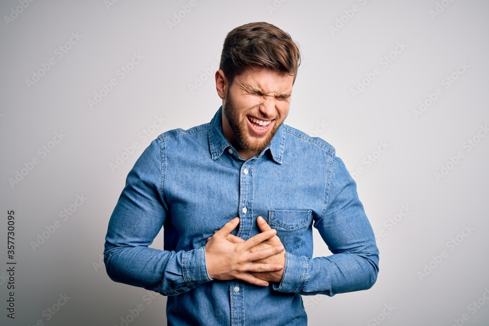 Young handsome blond man with beard and blue eyes wearing casual denim shirt smiling and laughing hard out loud because funny crazy joke with hands on body. Young handsome blond man with beard and blue eyes wearing casual denim shirt smiling and laughing hard out loud because funny crazy joke with hands on body.