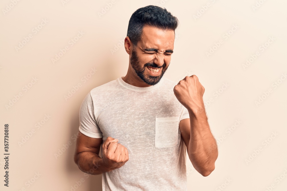 Fototapeta premium Young hispanic man wearing casual clothes celebrating surprised and amazed for success with arms raised and eyes closed