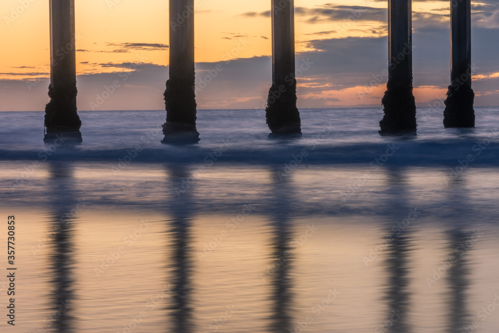 Pier posts reflecting on wet sand during sunset.