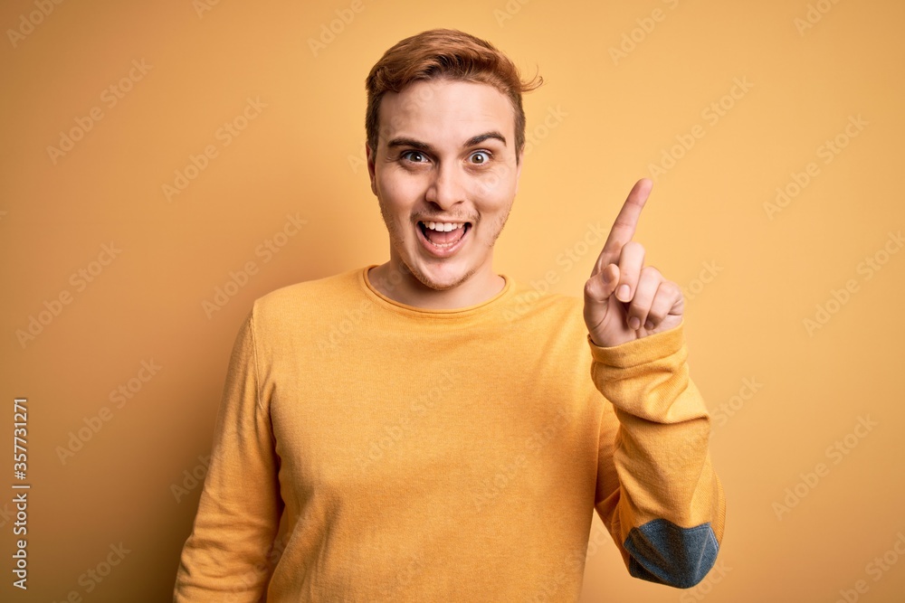 Young handsome redhead man wearing casual sweater over isolated yellow background pointing finger up with successful idea. Exited and happy. Number one. Young handsome redhead man wearing casual sweater over isolated yellow background pointing finger up with successful idea. Exited and happy. Number one.