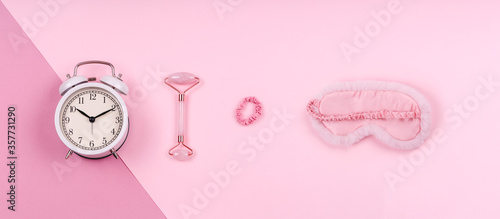 Pink drop with cute fluffy sleep mask, jade roller, watch and pink accessories. Sleep management and optimization, beauty sleep, beauty and sleep log concept. Place for text, banner format