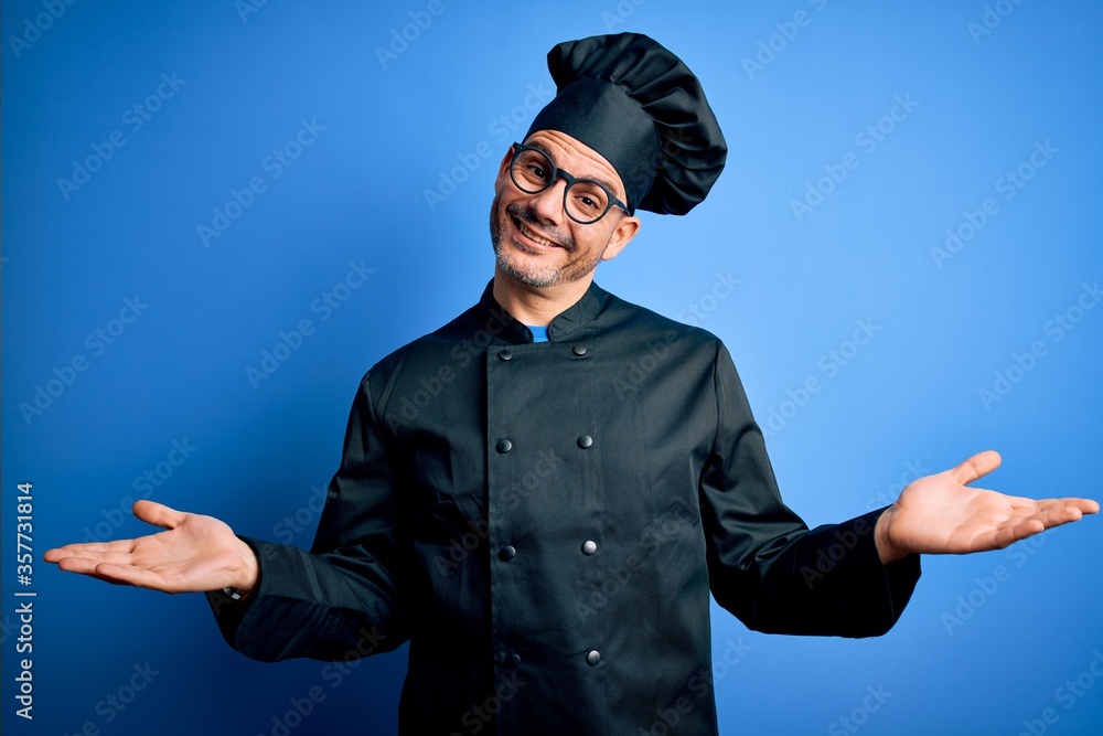 Young handsome chef man wearing cooker uniform and hat over isolated blue background smiling showing both hands open palms, presenting and advertising comparison and balance Young handsome chef man wearing cooker uniform and hat over isolated blue background smiling showing both hands open palms, presenting and advertising comparison and balance