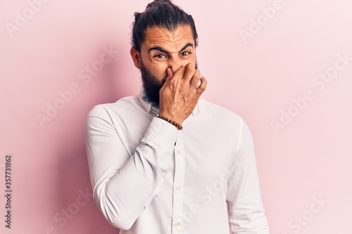 Young arab man wearing casual clothes smelling something stinky and disgusting, intolerable smell, holding breath with fingers on nose. bad smell