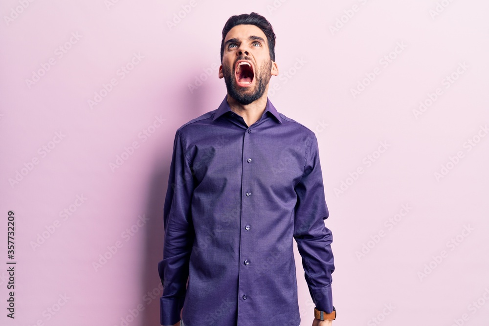 Fototapeta premium Young handsome man with beard wearing casual shirt angry and mad screaming frustrated and furious, shouting with anger. rage and aggressive concept.