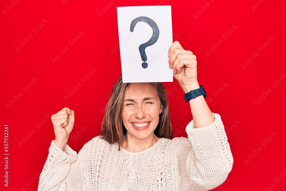 Young beautiful blonde woman holding question mark over head screaming proud, celebrating victory and success very excited with raised arm Young beautiful blonde woman holding question mark over head screaming proud, celebrating victory and success very excited with raised arm