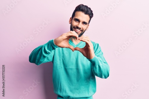 Young handsome man with beard wearing casual sweater smiling in love doing heart symbol shape with hands. romantic concept.