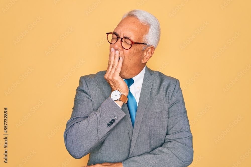 Middle age senior grey-haired handsome business man wearing glasses over yellow background bored yawning tired covering mouth with hand. Restless and sleepiness. Middle age senior grey-haired handsome business man wearing glasses over yellow background bored yawning tired covering mouth with hand. Restless and sleepiness.