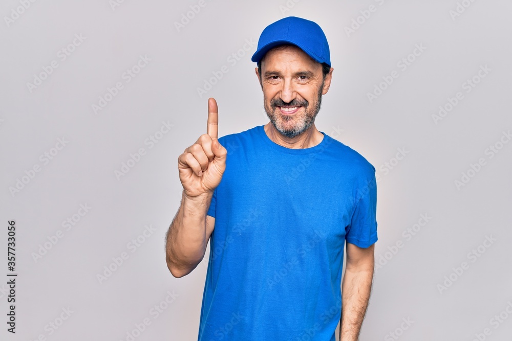 Fototapeta premium Middle age handsome deliveryman wearing cap standing over isolated white background smiling with an idea or question pointing finger up with happy face, number one