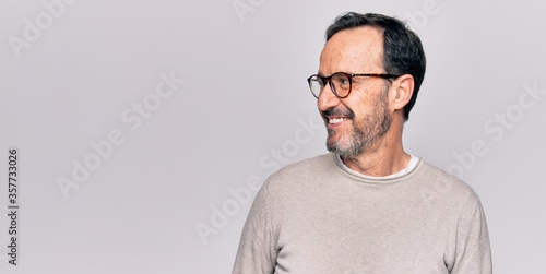 Middle age handsome man wearing casual sweater and glasses over isolated white background looking to side, relax profile pose with natural face and confident smile.