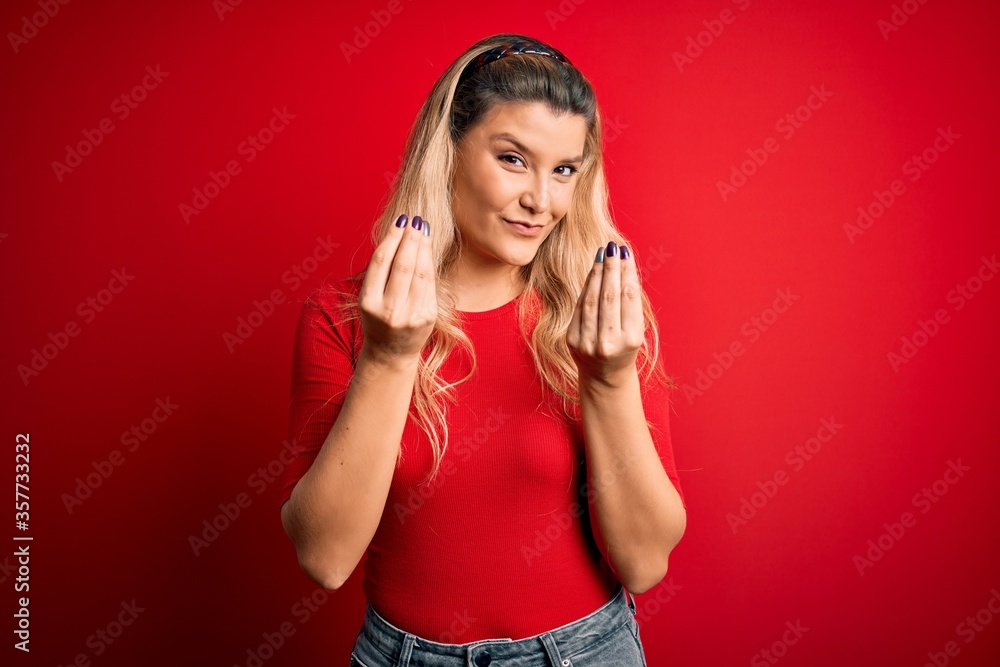 Fototapeta premium Young beautiful blonde woman wearing casual t-shirt standing over isolated red background doing money gesture with hands, asking for salary payment, millionaire business