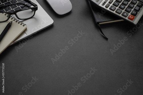Dark grey office desk table with laptop, glasses with notebook and equipment other office supplies.