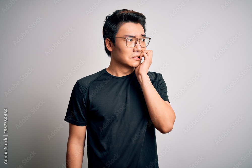 Young handsome chinese man wearing black t-shirt and glasses over white background looking stressed and nervous with hands on mouth biting nails. Anxiety problem. Young handsome chinese man wearing black t-shirt and glasses over white background looking stressed and nervous with hands on mouth biting nails. Anxiety problem.