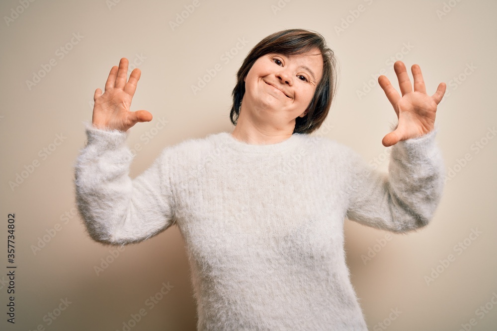 Young down syndrome woman standing over isolated background showing and pointing up with fingers number ten while smiling confident and happy.
