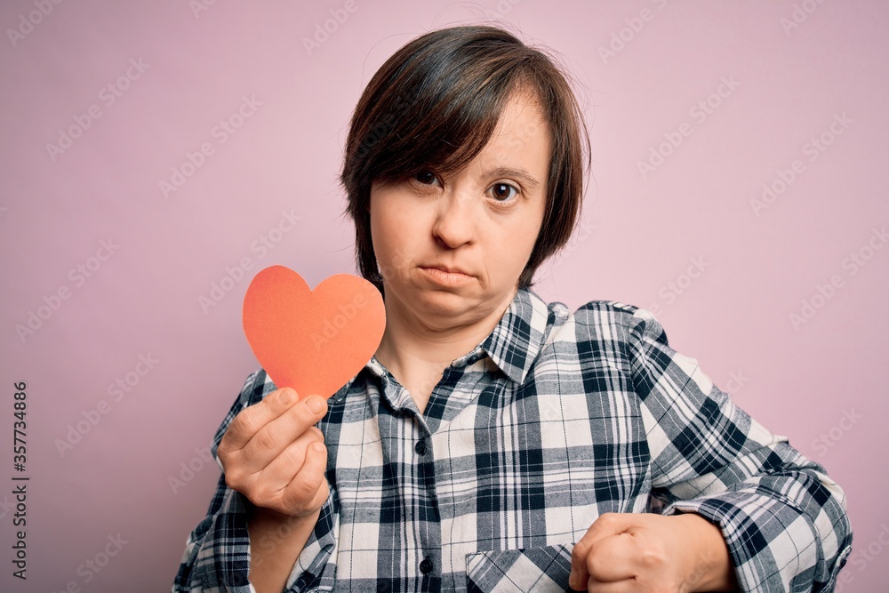 Young down syndrome romantic woman holding red heart paper shape over pink background annoyed and frustrated shouting with anger, crazy and yelling with raised hand, anger concept Young down syndrome romantic woman holding red heart paper shape over pink background annoyed and frustrated shouting with anger, crazy and yelling with raised hand, anger concept